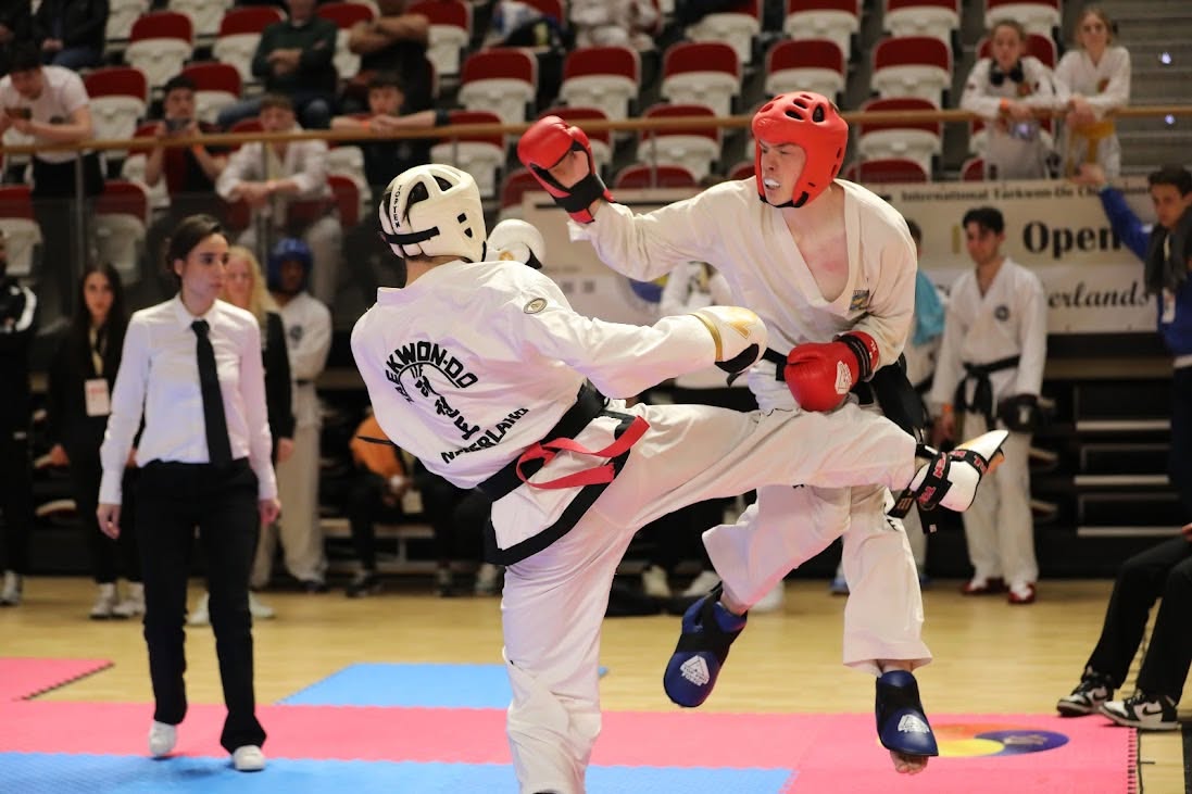 Two ITF Taekwon-Do competitors mid-air trading kicks in a championship ring