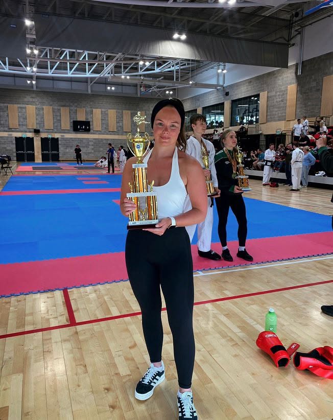 Club member holding a championship trophy beside the mats